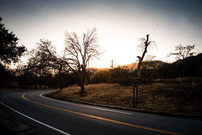 Road by trees against sky during sunset