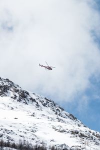 Low angle view of airplane flying over snowcapped mountains against sky