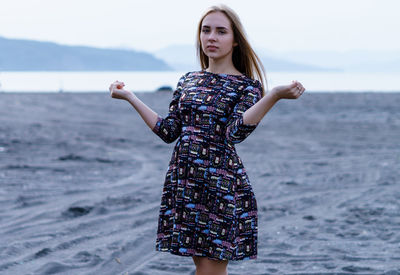 Portrait of young woman standing at beach against sky