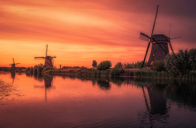 Traditional windmill by lake against sky during sunset