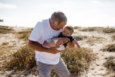 Grandfather cradling grandson while standing on beach