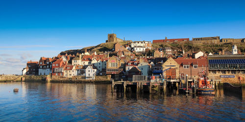 Buildings by river against blue sky