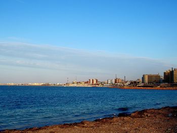 Scenic view of sea and buildings against blue sky