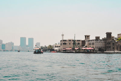 Boats sailing on sea by buildings against clear sky