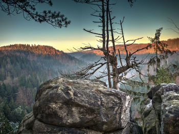 Rock by lake against sky during sunset