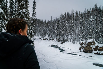 Female over shoulder view looking out at snowy landscape and forest in canada.