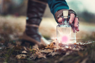 Low section of woman holding illuminated liquid in jar on field