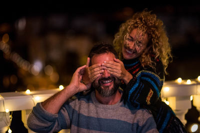 Smiling woman closing eyes of man from behind at night