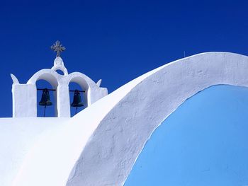 Low angle view of bells on whitewashed church against clear blue sky