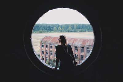 Rear view of backpack woman sitting on circle shaped building window