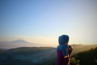 Rear view of woman standing on mountain against sky