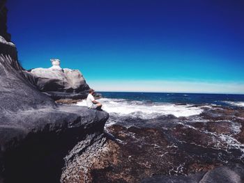 Rock formation in sea against clear blue sky