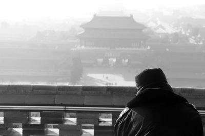 Rear view of person by traditional house during foggy weather