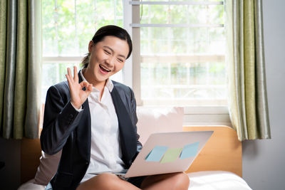 Young woman using phone while standing on window