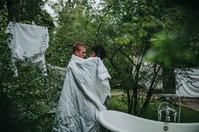 Couple with towel standing against trees