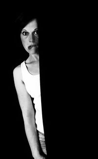 Close-up portrait of young woman standing against black background