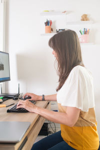 Side view of woman using phone while sitting on table