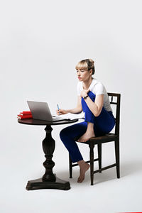 Young woman using laptop while sitting on chair against white background