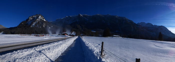 Panoramic view of road amidst snowy field leading towards mountains on sunny day