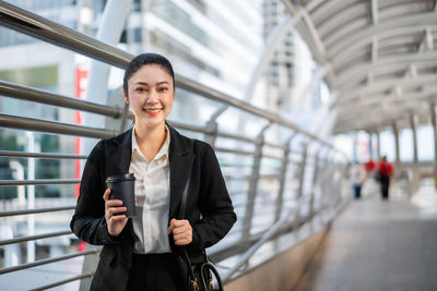 Full length portrait of businesswoman holding coffee cup on footpath in city