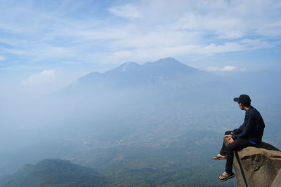 Man sitting on mountain against sky