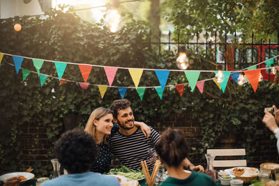 Smiling male and female friends posing for photograph during dinner party in backyard