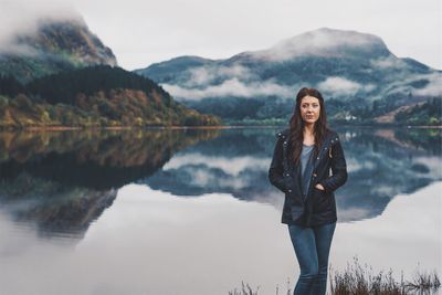 Portrait of smiling young woman standing by lake against mountains