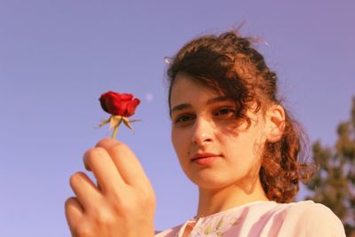 Portrait of young woman holding red flowering plant against sky