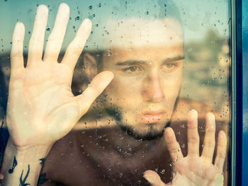 Close-up portrait of man looking through wet glass window