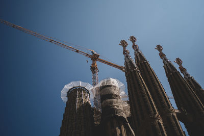 Low angle view of crane by building against clear blue sky