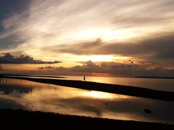 Distant view of silhouette man walking at beach against sky during sunset