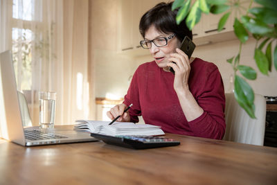 Young woman using mobile phone while sitting on table