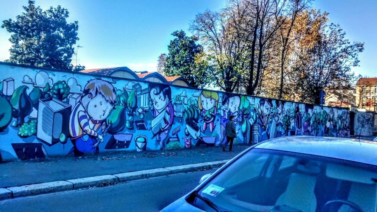 graffiti, blue, transportation, clear sky, text, tree, western script, built structure, art, art and craft, architecture, creativity, sky, sunlight, land vehicle, outdoors, day, road, low angle view, no people