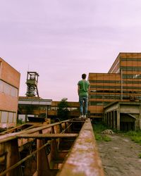 Rear view of man standing by building against sky