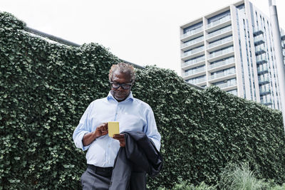 Businessman using mobile phone while standing in front of green wall