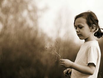 Side view of girl holding dead plant while standing outdoors