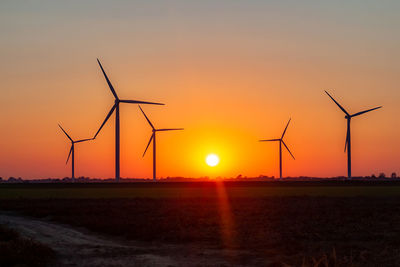 Silhouette wind turbines on field against sky during sunset