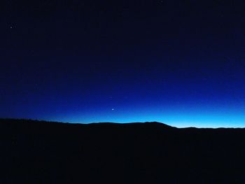 Silhouette landscape against clear blue sky at night