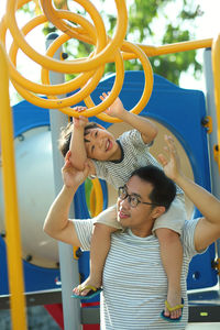 Father assisting son in climbing jungle gym standing on playground