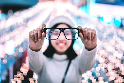 Young woman holding eyeglasses against illuminated lights