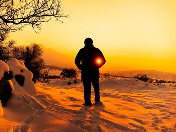 Rear view of silhouette man standing on snow covered land