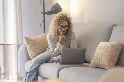 Woman using phone while sitting on sofa at home