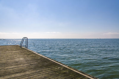 Scenic view of wooden deck with ladder by sea against sky