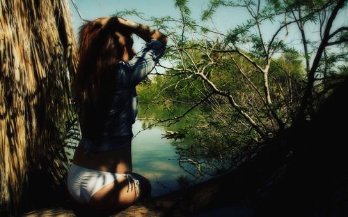 Woman sitting by tree against sky