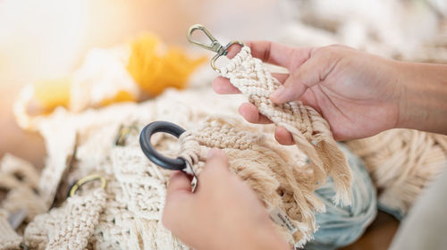 Female hands choosing the hand-made macrame beige thread hanger with stainless keychain.