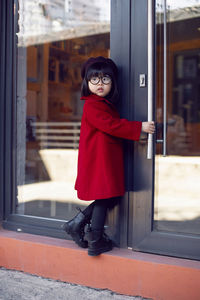 Korean girl in a red coat and beret stands on the street against at the glass doors of the store