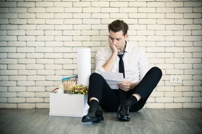 Young man using mobile phone while sitting on wall