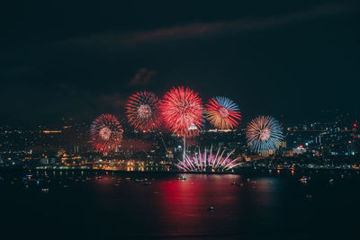 Firework display over illuminated city against sky at night