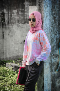 Young woman wearing sunglasses standing against pink wall