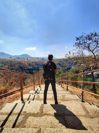 Rear view of man standing on railing against sky